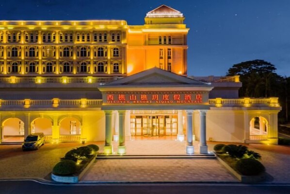 A large, illuminated hotel with a grand entrance, multiple balconies, and a prominent sign. - Xiqiao Mountain Qiaoyue Resort Hotel (Foshan)