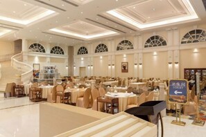 A spacious hotel lobby with multiple dining areas, a staircase, and a sign indicating the location of the restroom.