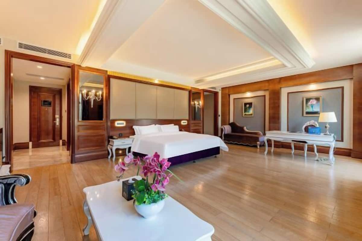 A hotel room with a bed, bedside table, chair, desk, and a potted plant.