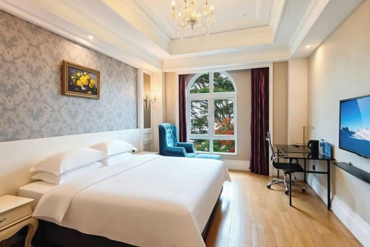 A hotel room with a bed, a desk, a chair, a television, and a window with curtains.