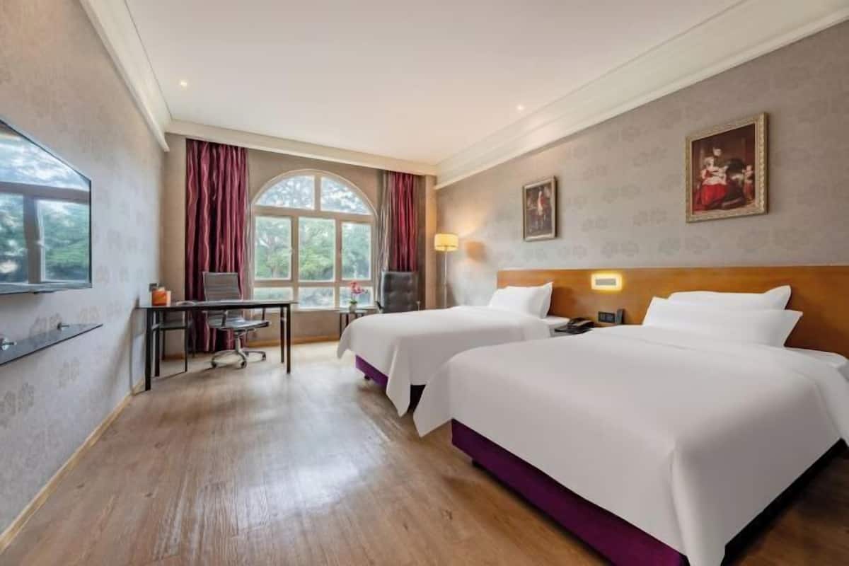 A hotel room with two beds, a desk, a chair, a TV, and a window with curtains.