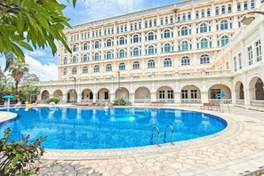 A large pool surrounded by a building with multiple arches and a tiled floor. - Xiqiao Mountain Qiaoyue Resort Hotel (Foshan)