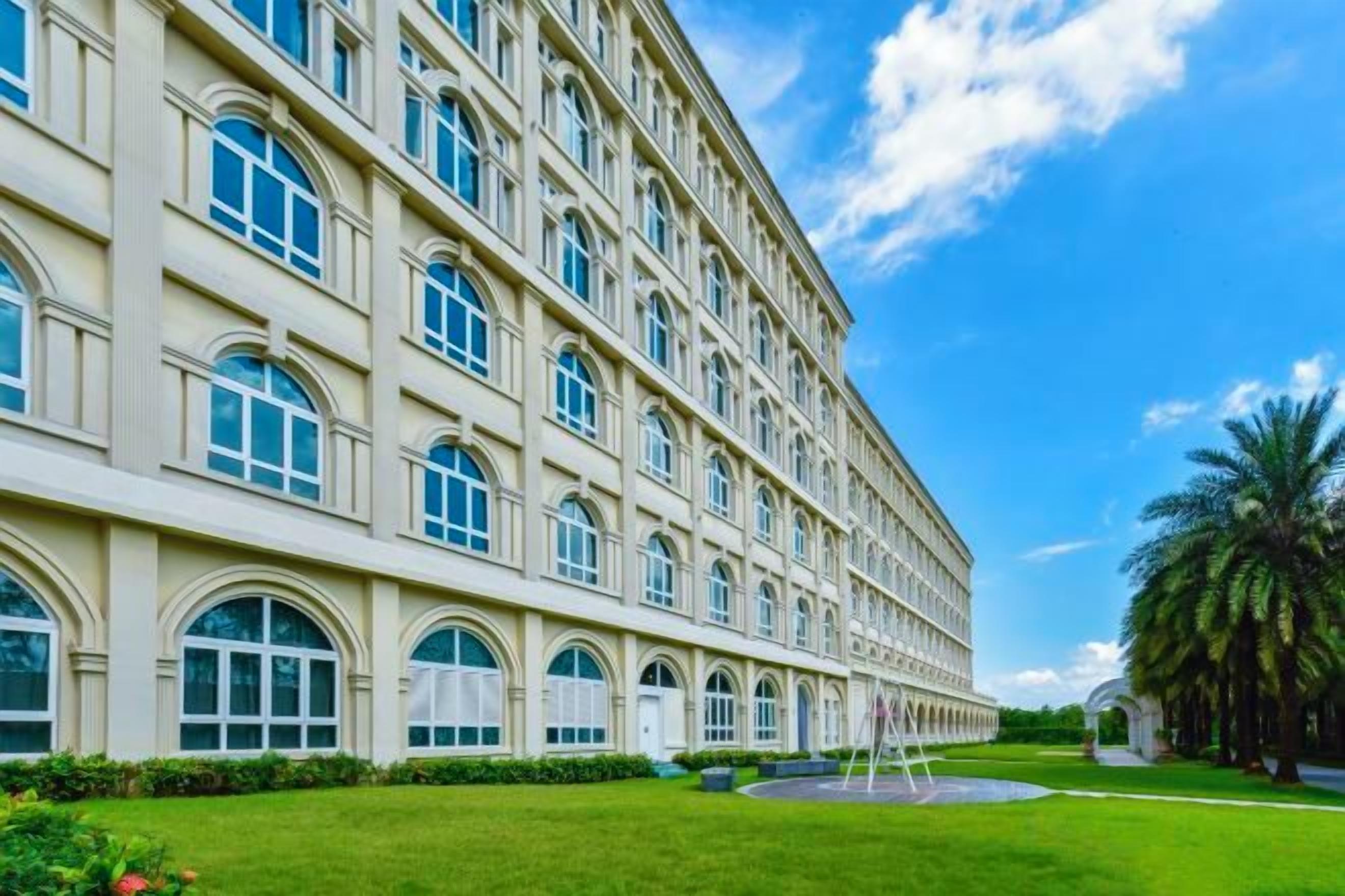 A large, multi-story building with a symmetrical facade, arched windows, and a well-maintained lawn.