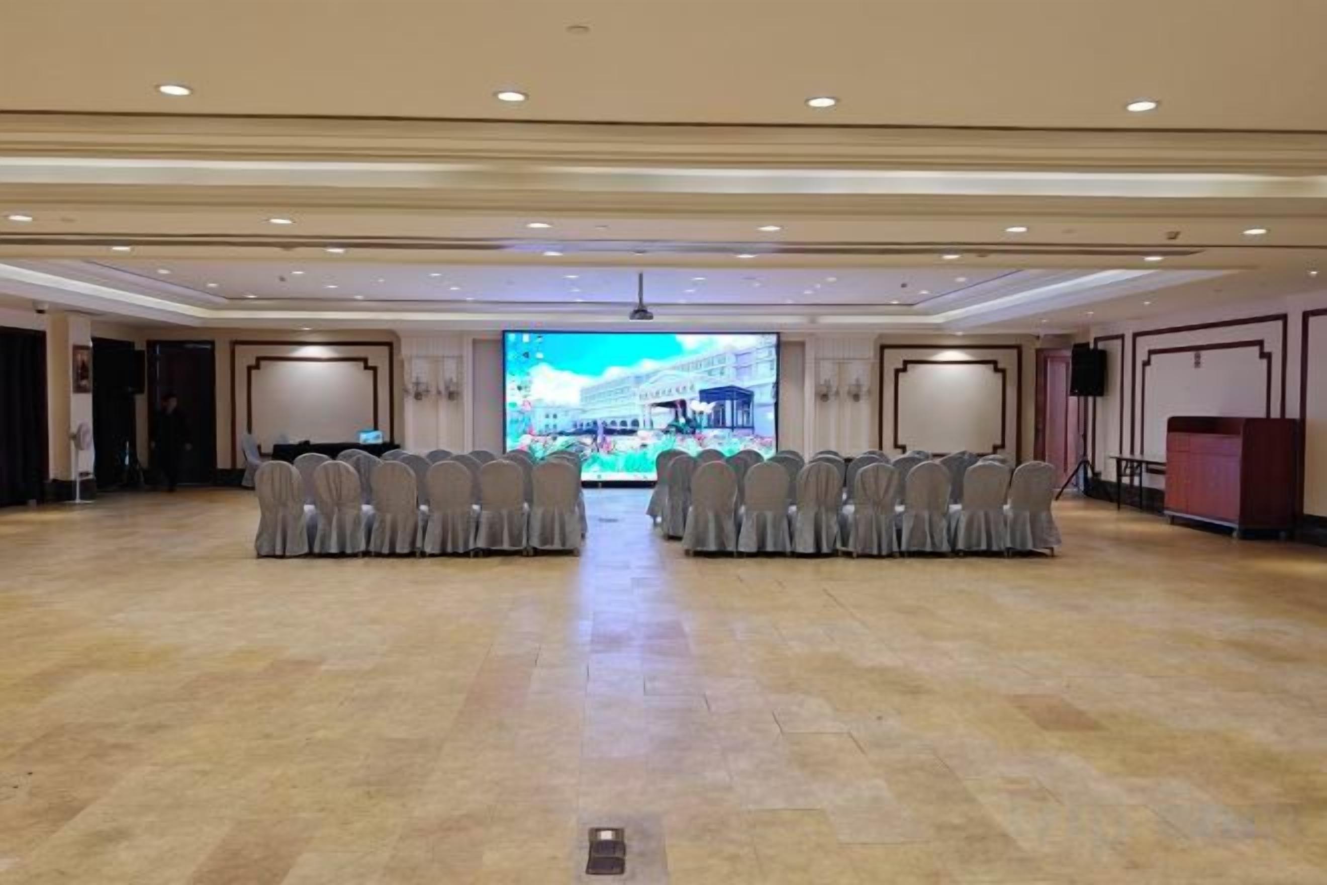 Une salle de conférence avec des rangées de chaises, une scène et un grand écran.