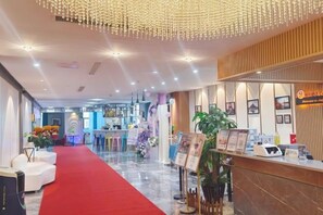 A hotel lobby with a red carpet, reception desk, and decorative plants. - Campanile Hotel (Zhuji)