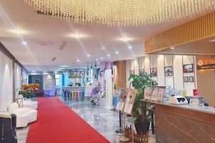 Um saguão de hotel com carpete vermelho, balcão de recepção e plantas decorativas.