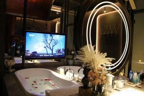 A modern bathroom with a large mirror, a bathtub with rose petals, and a television. - Campanile Hotel (Zhuji)