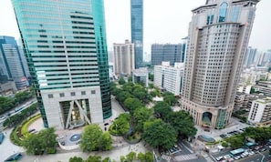 Un edificio moderno de gran altura con fachada de vidrio, rodeado de vegetación y otros edificios.