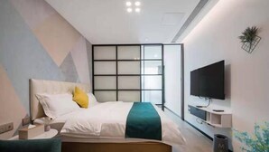 Een moderne hotelkamer met een bed, een televisie, een bureau en een plant.
