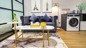 Un salon moderne comprenant un canapé, une table basse, un lave-linge et deux tableaux encadrés représentant des monuments célèbres.