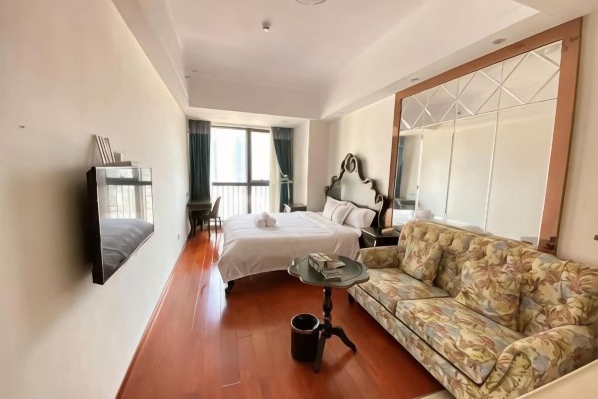 Een hotelkamer met een bed, een sofa, een televisietoestel en een raam.