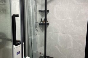 Eine Duschkabine mit Glastüren, geflieste Wände und Ablage für Toilettenartikel.