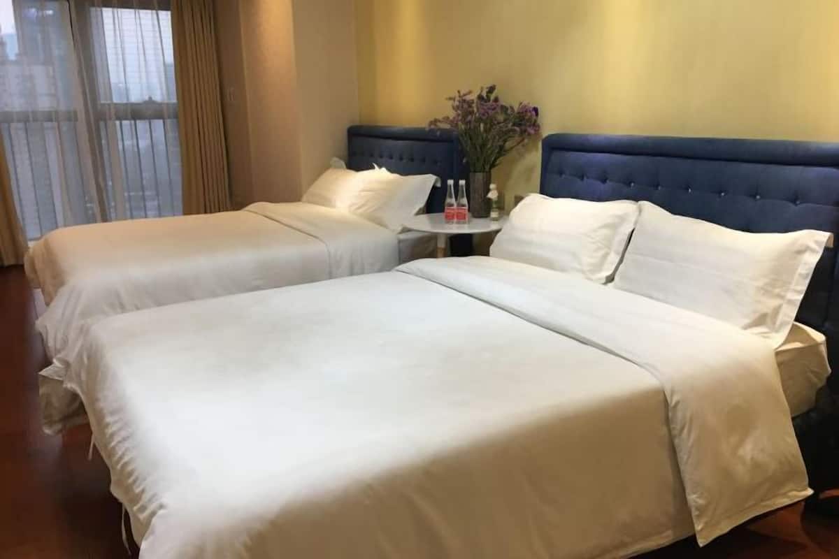 Een hotelkamer met twee bedden, een klein tafeltje met een bloevas, en uitzicht door dunne gordijnen.