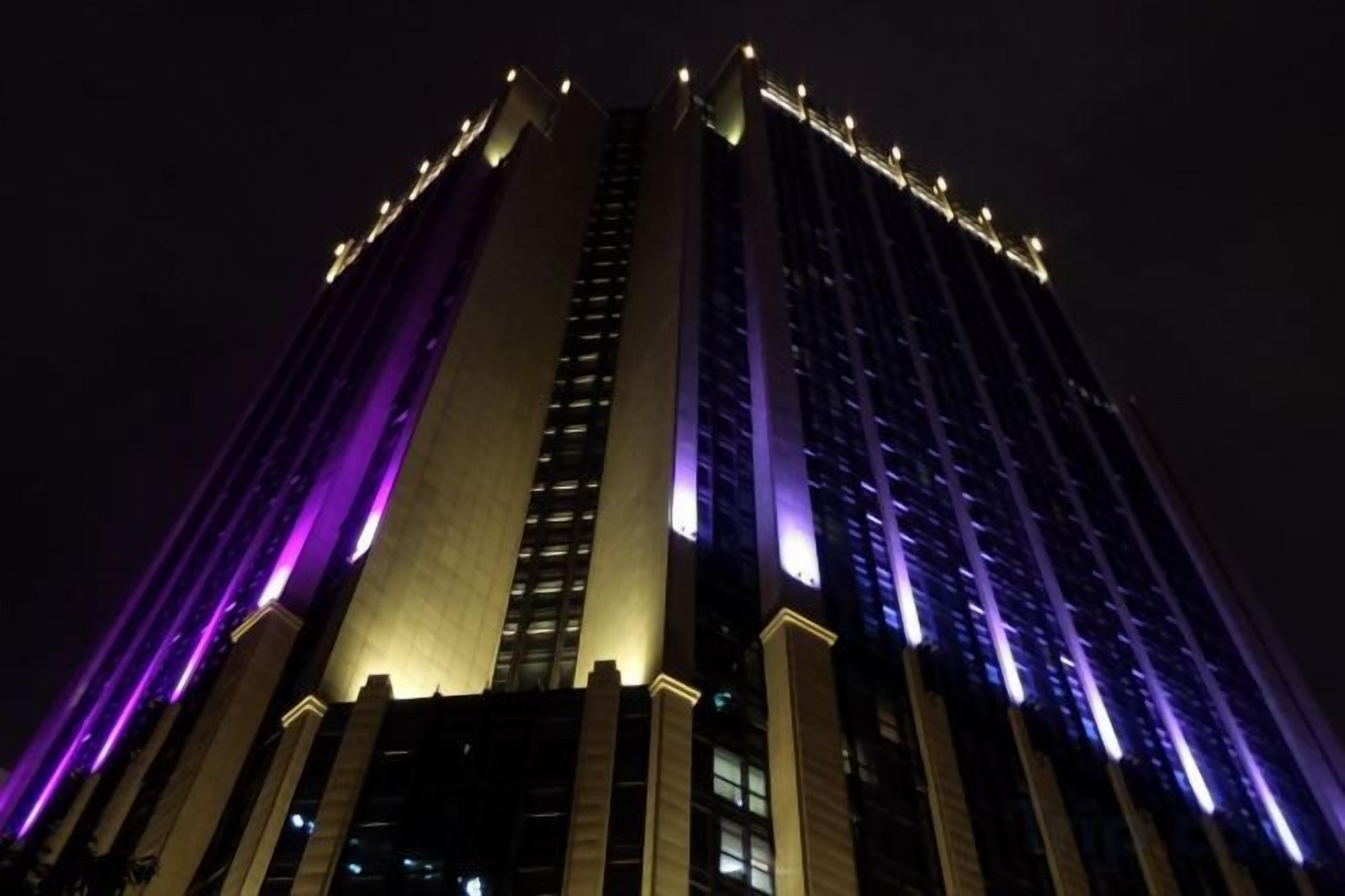 Um edifício alto com janelas iluminadas e uma faixa vertical de luz destacada em uma lateral.