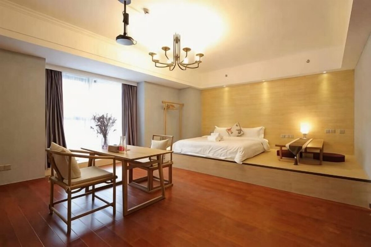 Een hotelkamer met een houten vloer, een bed met witte lakens, een eettafel met stoelen en een kroonluchter.