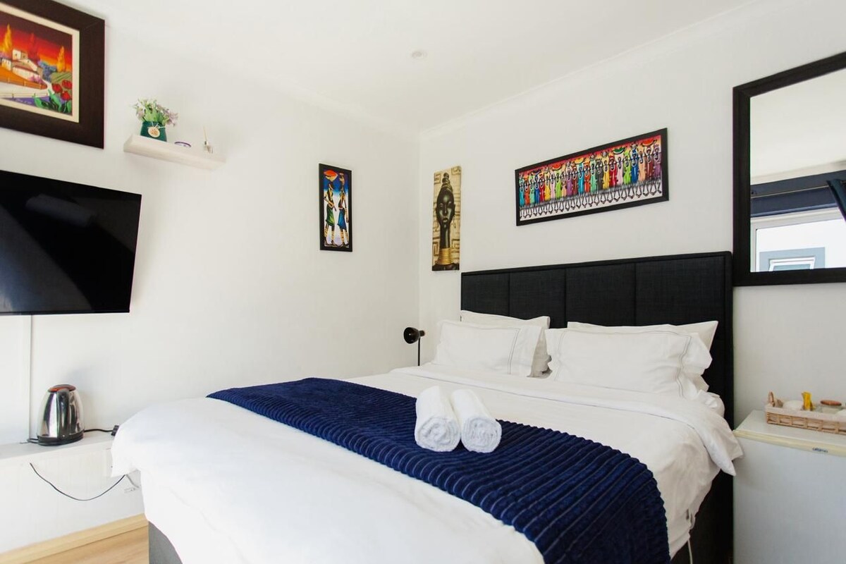 A hotel room with a bed, a flat-screen TV, a coffee maker, and artwork on the walls.