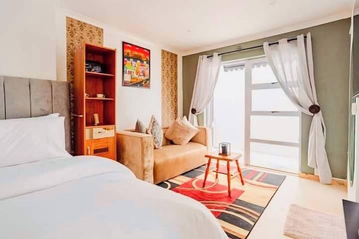 A bedroom with a bed, a sofa, a small table, and a bookshelf.