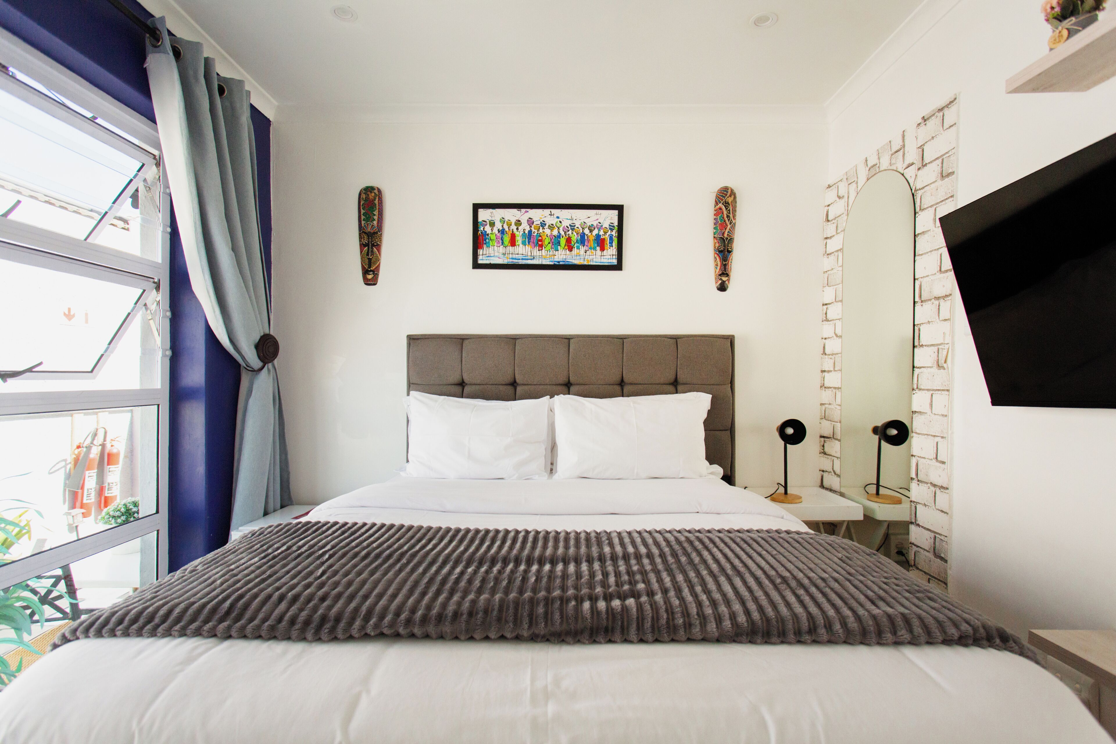 Een hotelkamer met een bed, een raam met gordijnen, een ingelijst schilderij aan de muur en een aan de muur bevestigde televisie.