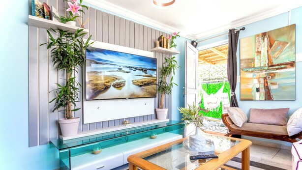 A living room with a TV mounted on the wall, a glass coffee table, a sofa, and a chair. - Caline VIP Mews (Cape Town)
