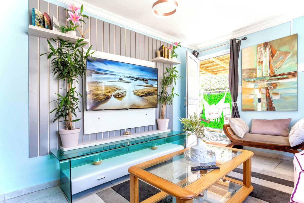A living room with a TV mounted on the wall, a glass coffee table, a sofa, and a chair.