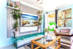 A living room with a TV mounted on the wall, a glass coffee table, a sofa, and a chair. - Caline VIP Mews (Cape Town)