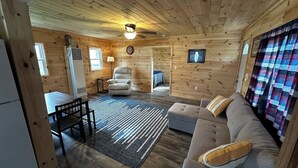 A cozy cabin interior with a wooden ceiling, a ceiling fan, a sofa, a chair, a table, and a rug. - Bear Lake | Hot Tub, Kayaks, Firepit, Lake & Beach (Lake)