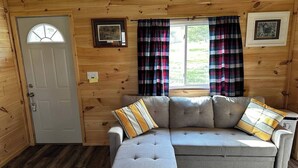 A cozy cabin interior with a gray sofa, plaid curtains, and wooden walls. - Bear Lake | Hot Tub, Kayaks, Firepit, Lake & Beach (Lake)