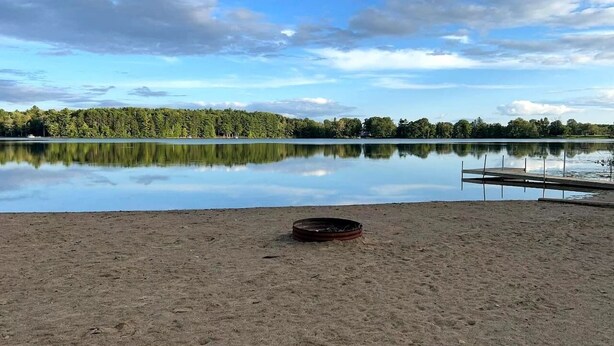 A sandy beach with a calm lake, a wooden dock, and a forest in the background. - Bear Lake | Hot Tub, Kayaks, Firepit, Lake & Beach (Lake)