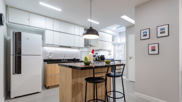 Une cuisine moderne avec des meubles blancs, un îlot central doté de tabourets, un réfrigérateur et un luminaire suspendu.