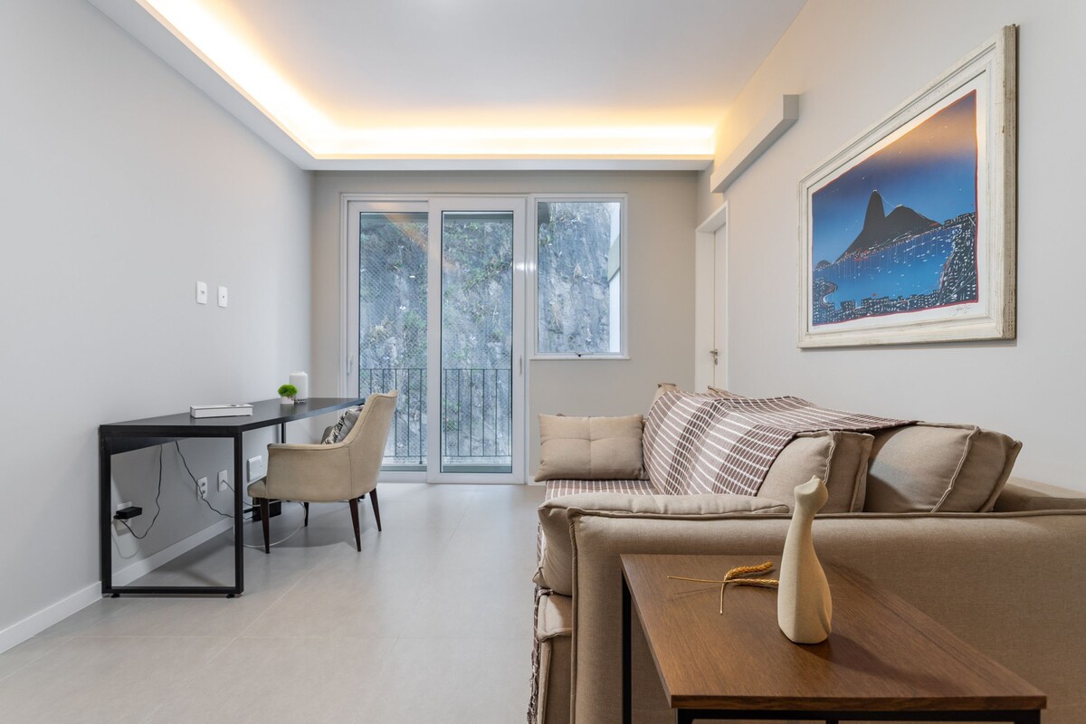 Una sala de estar moderna con un sofá, una mesa de comedor y una silla. Hay un ventanal con vistas a árboles.