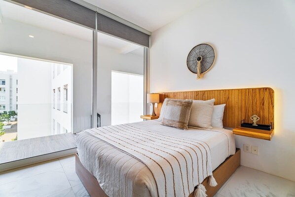 Un dormitorio moderno con una cama grande, cabecera de madera, ventilador de pared y vista a un balcón.