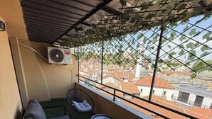 En balkong med en soffa och två små bord, en luftkonditioneringsanläggning och utsikt över byggnader.