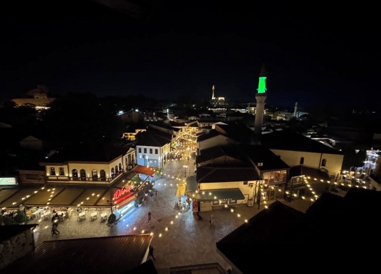 Een nachtzicht van een plein met verlichte gebouwen en een opvallende toren met een groen licht.