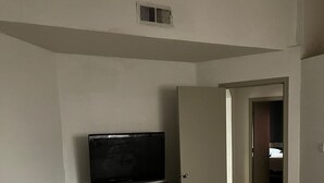 Ein Schlafzimmer mit einem Bett, einem Fernseher auf einer Kommode und einer Tür zu einem anderen Raum.
