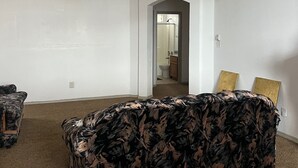 Ein Wohnzimmer mit einer gemusterten Couch, einem Deckenventilator und Blick in das Badezimmer durch einen Bogen.