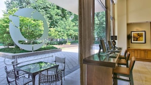 Un hall d’hôtel moderne avec une grande table et des chaises en verre, un comptoir d’accueil et une vue sur un espace extérieur verdoyant agrémenté d’une grande sculpture décorative.