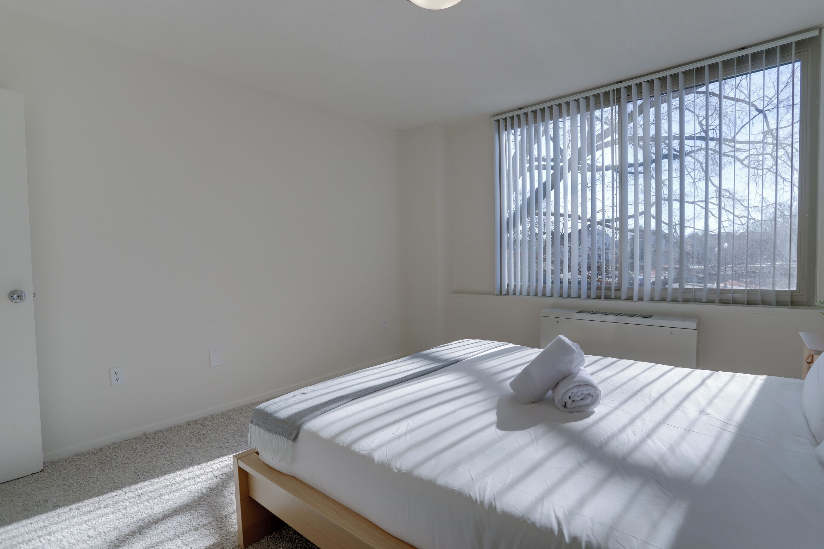 Une chambre d’hôtel propre et minimaliste, avec un lit simple, une fenêtre avec des stores et un radiateur.