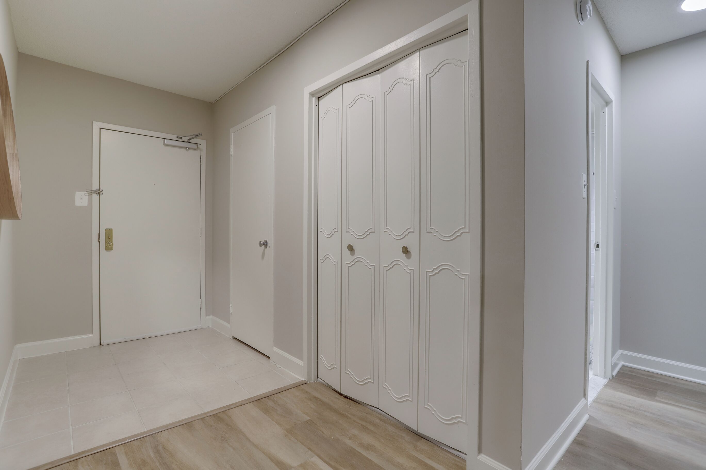 A hallway with a white door, a white wardrobe with decorative panels, and a light-colored floor.