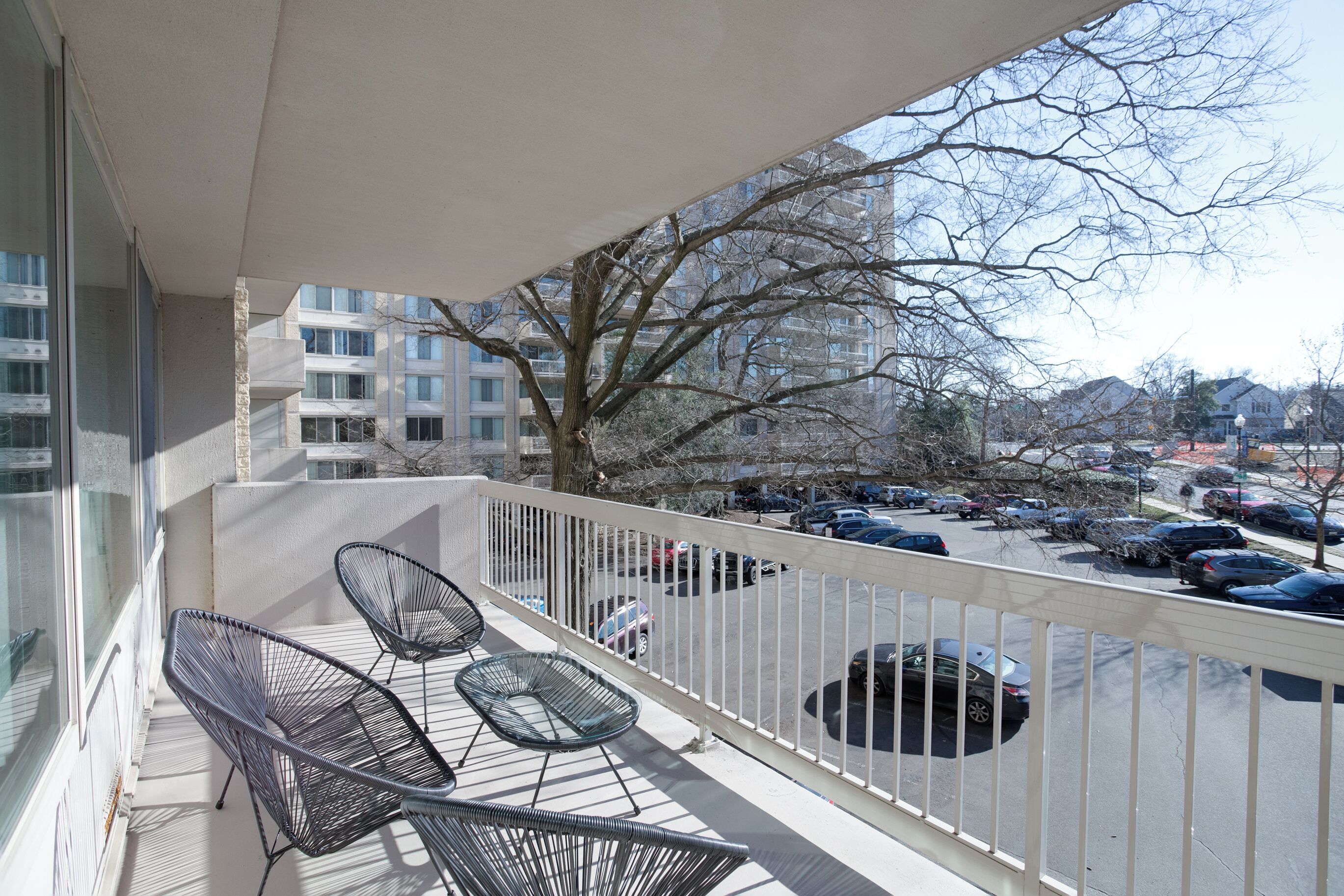 Een balkon met twee stoelen en uitzicht op een parkeerplaats en een boom.