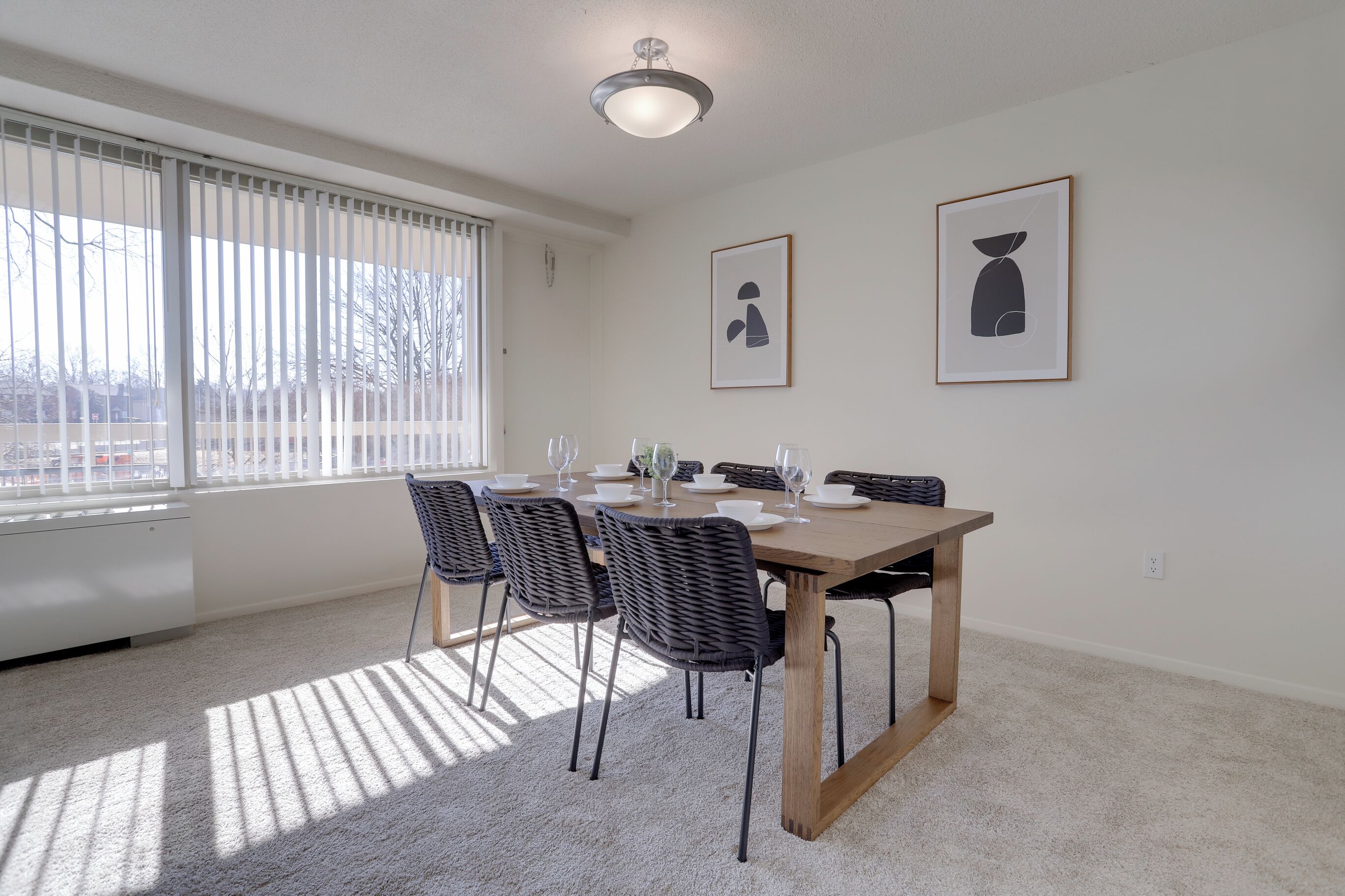 A dining area with a wooden table, black chairs, and framed artwork on the wall.