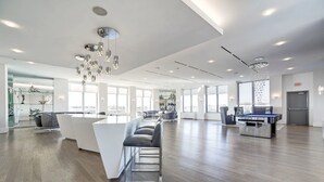 Un hall d’hôtel spacieux et moderne, doté d’un comptoir d’accueil central, d’un espace salon et de grandes fenêtres offrant une vue sur la ville.
