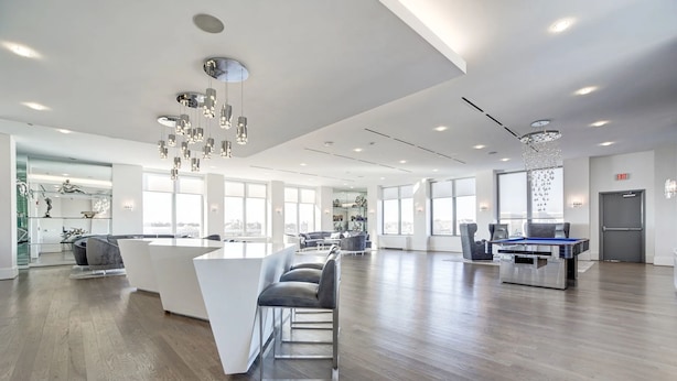 Un hall d’hôtel spacieux et moderne, doté d’un comptoir d’accueil central, d’un espace salon et de grandes fenêtres offrant une vue sur la ville.