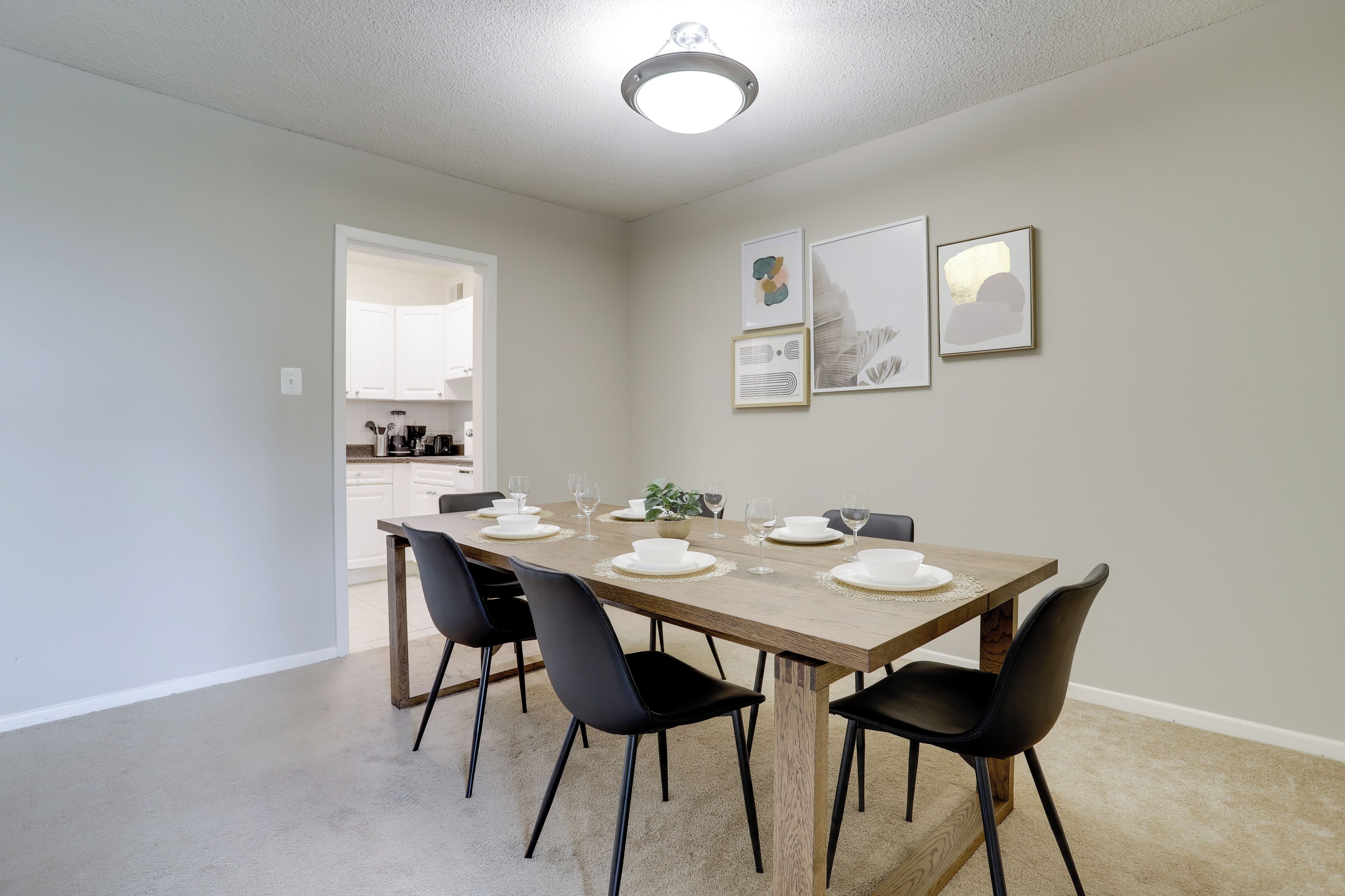 A dining area with a wooden table set for four, black chairs, and framed artwork on the wall.