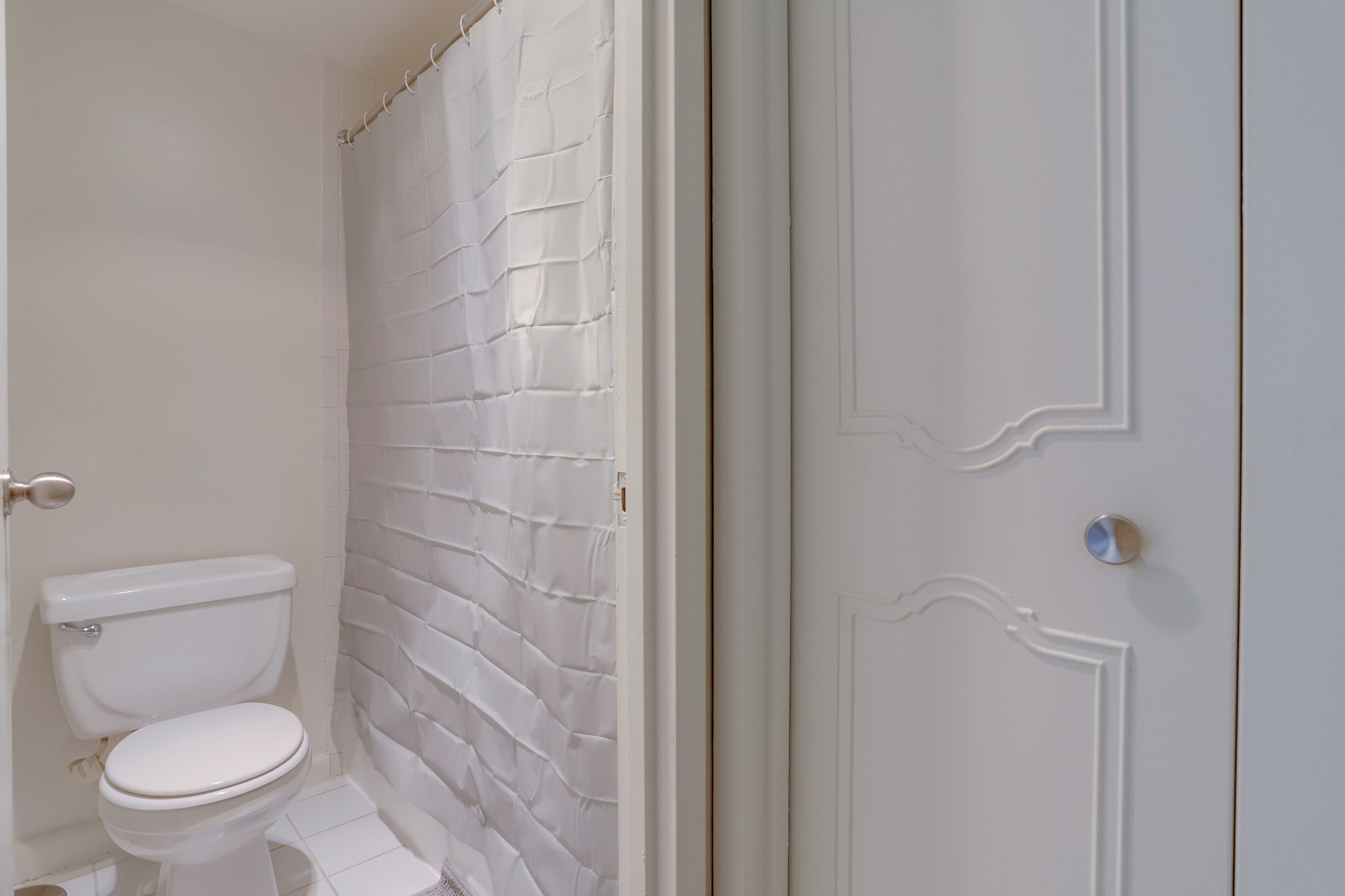Un baño con inodoro blanco, cortina de ducha y puerta blanca con picaporte.