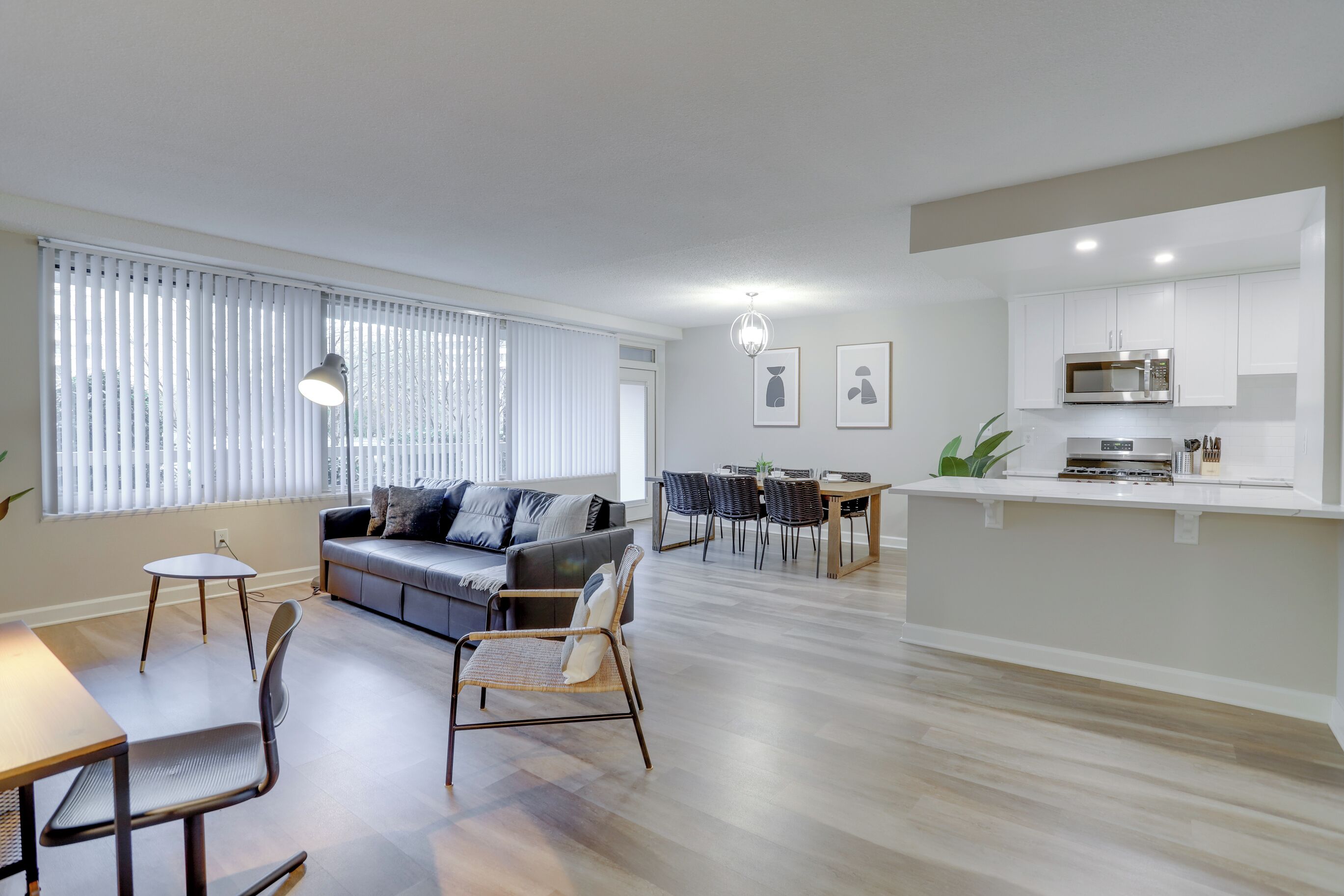 Een moderne woonkamer met een bank, stoelen, een eettafel en een keuken met kasten en apparatuur.