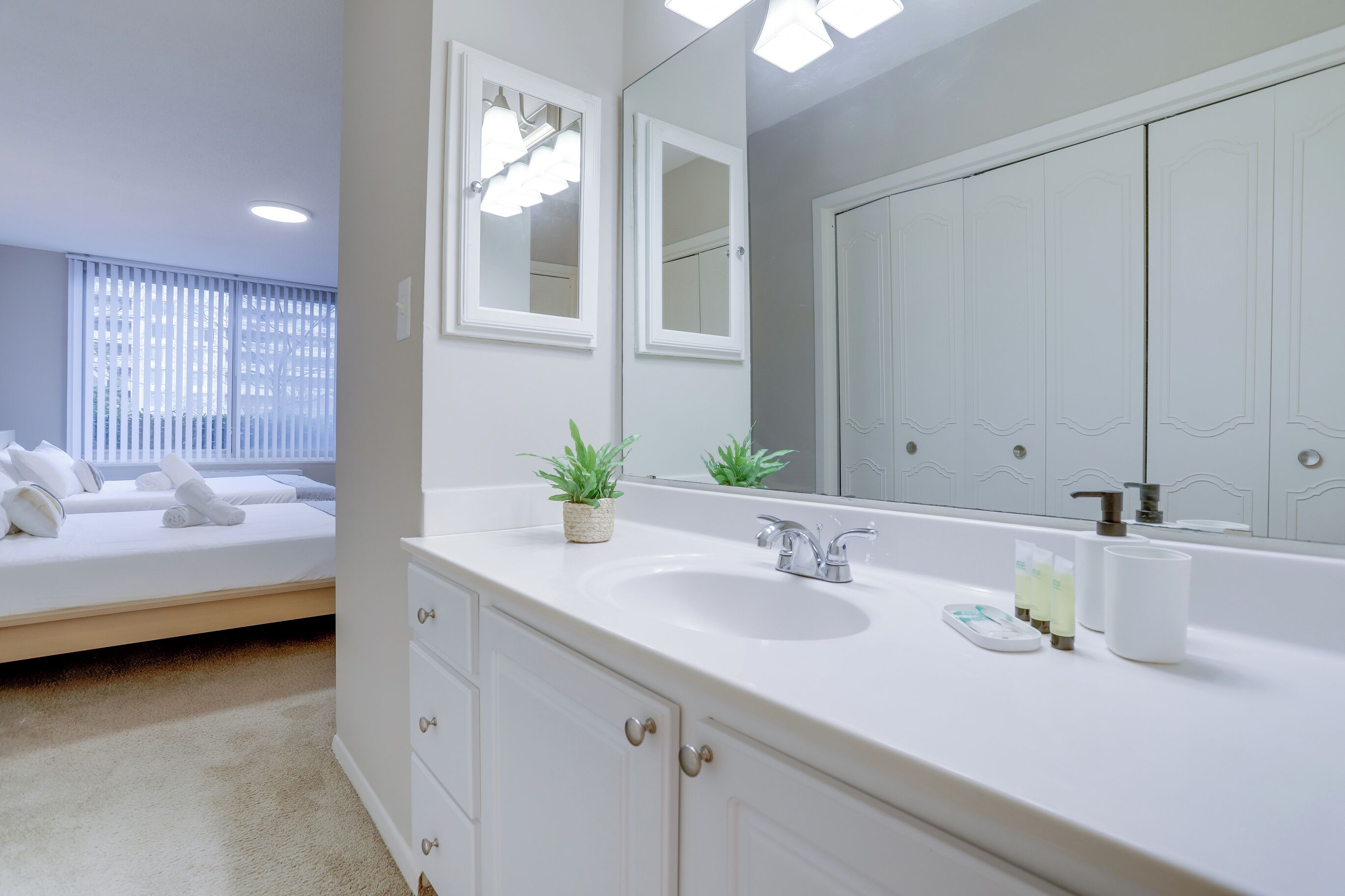 A modern bathroom with a large mirror, white sink, and a bed with neatly made towels.