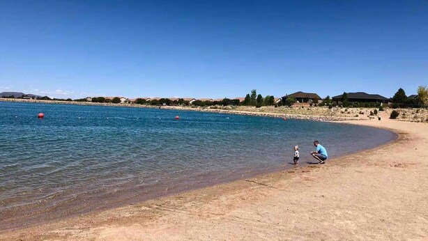 Une plage avec une eau d’un bleu limpide, un rivage sablonneux et des maisons en arrière-plan.