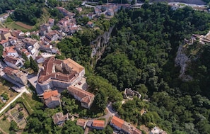 Vue aérienne d’une ville historique, avec un imposant édifice ressemblant à un château, entouré de bâtiments résidentiels et de vastes zones boisées.