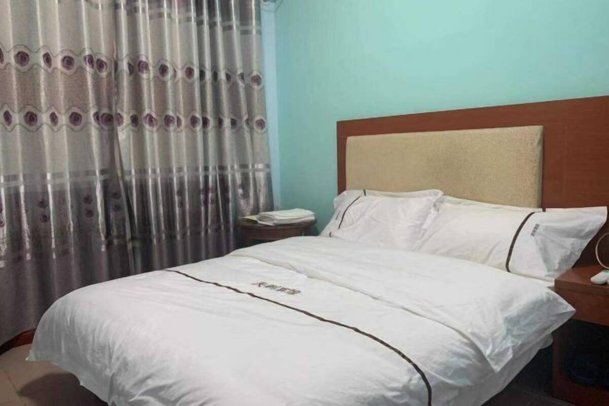 Een hotelkamer met een bed, nachtkastje, telefoon en raam met gordijnen.