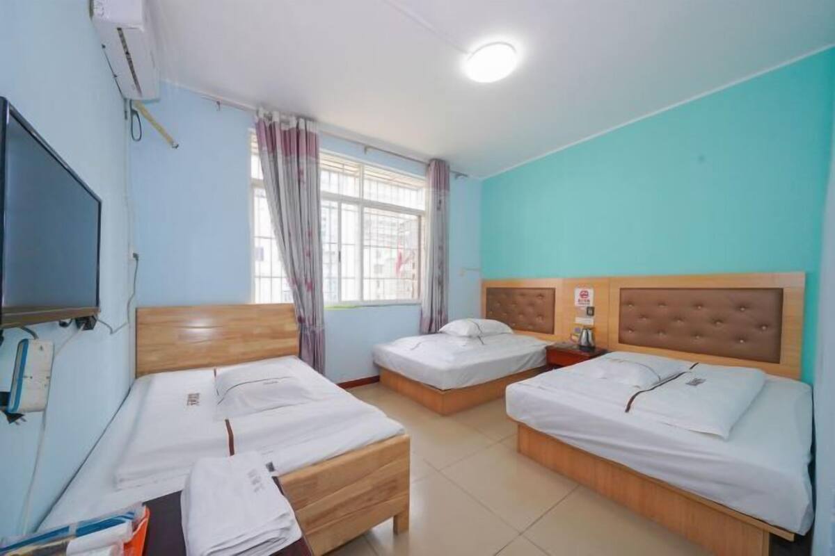 Een hotelkamer met drie eenpersoonsbedden, een televisie, een raam met gordijnen en een plafondlamp.